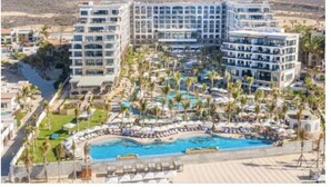 Ein Resort mit mehreren Gebäuden, einem zentralen Poolbereich und Palmen.