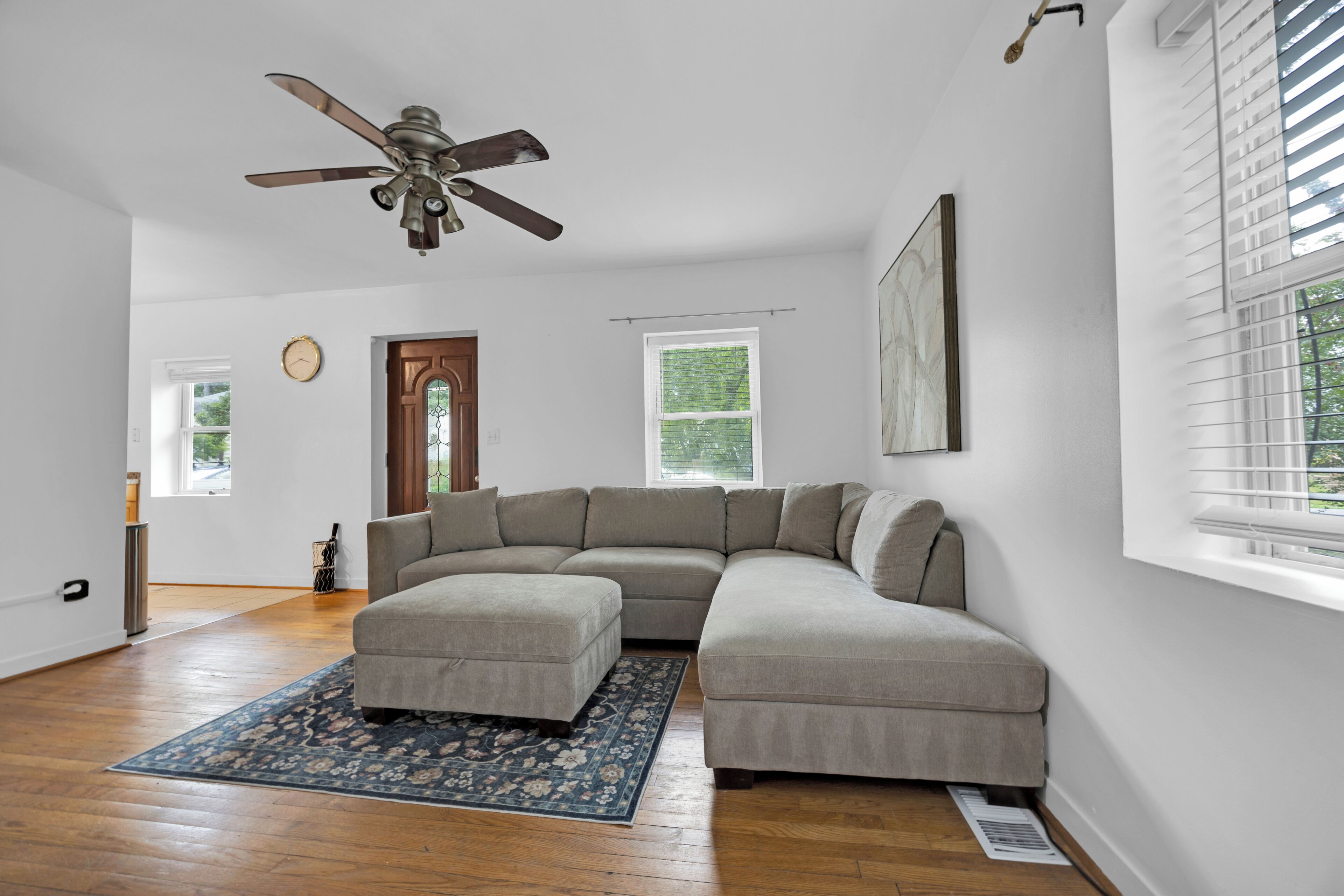 A modern living room with a sectional sofa, a ceiling fan, and a large window with blinds.