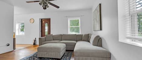 Una sala de estar moderna con un sofá modular, un ventilador de techo y un ventanal con persianas.