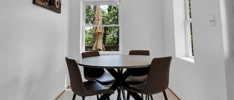 A dining area with a table and chairs, a ceiling fan, a window with a view of trees, and a painting on the wall.
