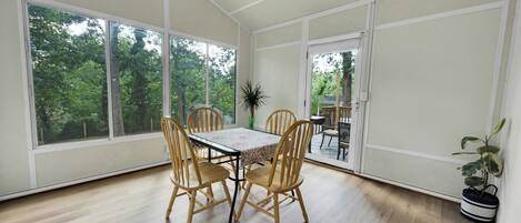 A dining area with a table and chairs, large windows, and a view of trees.