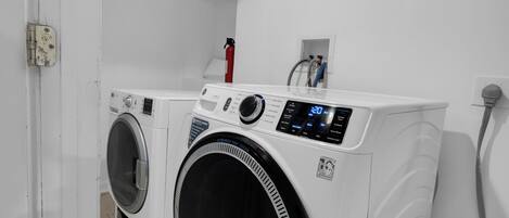 A modern laundry room with a front-loading washing machine and dryer, a fire extinguisher, and a visible electrical outlet.