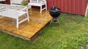 A red barn with a wooden deck, white benches, a grill, and a small window. - Amundtorp vandrarhem  (Hastveda)