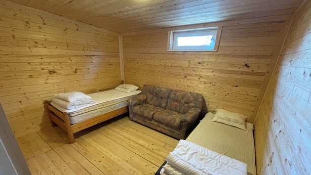 A cabin room with two beds, a sofa, wooden walls, and a skylight. - Amundtorp vandrarhem  (Hastveda)