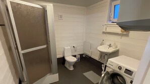 A compact bathroom with a toilet, sink, and washing machine. - Amundtorp vandrarhem  (Hastveda)