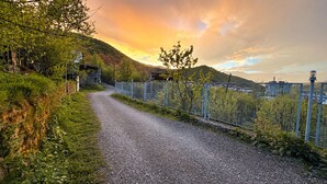 A gravel path bordered by a metal fence, leading to a hilly landscape with a sunset. - Spacious Forest Guesthouse in Vanadzor (Vanadzor)