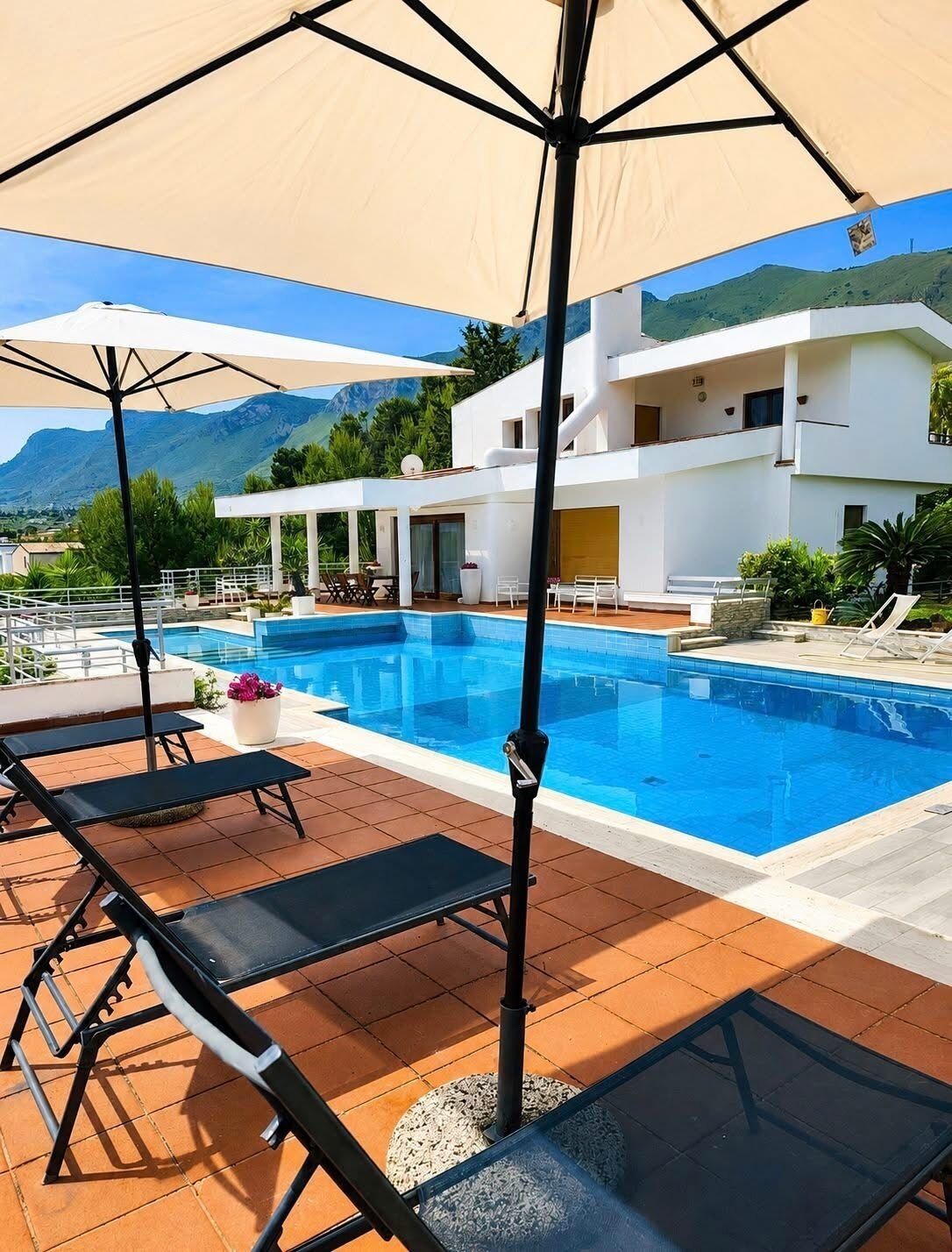 Un espace aménagé au bord de la piscine, avec des chaises longues, une piscine et un bâtiment moderne en arrière-plan.