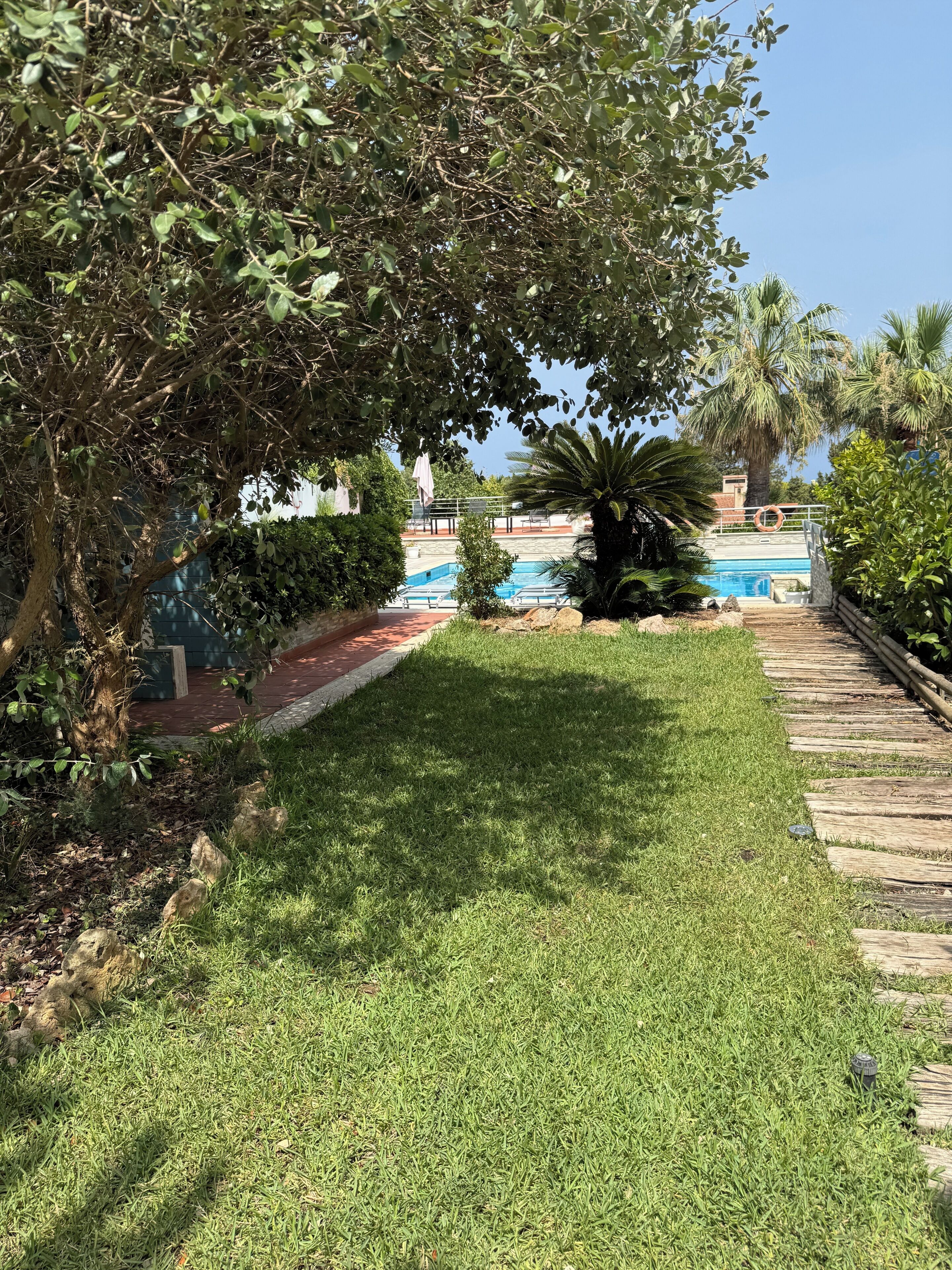 A pool area with a clear view of the water, surrounded by greenery and a wooden deck.