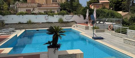 A swimming pool with a tiled deck, surrounded by potted plants and a white wall.