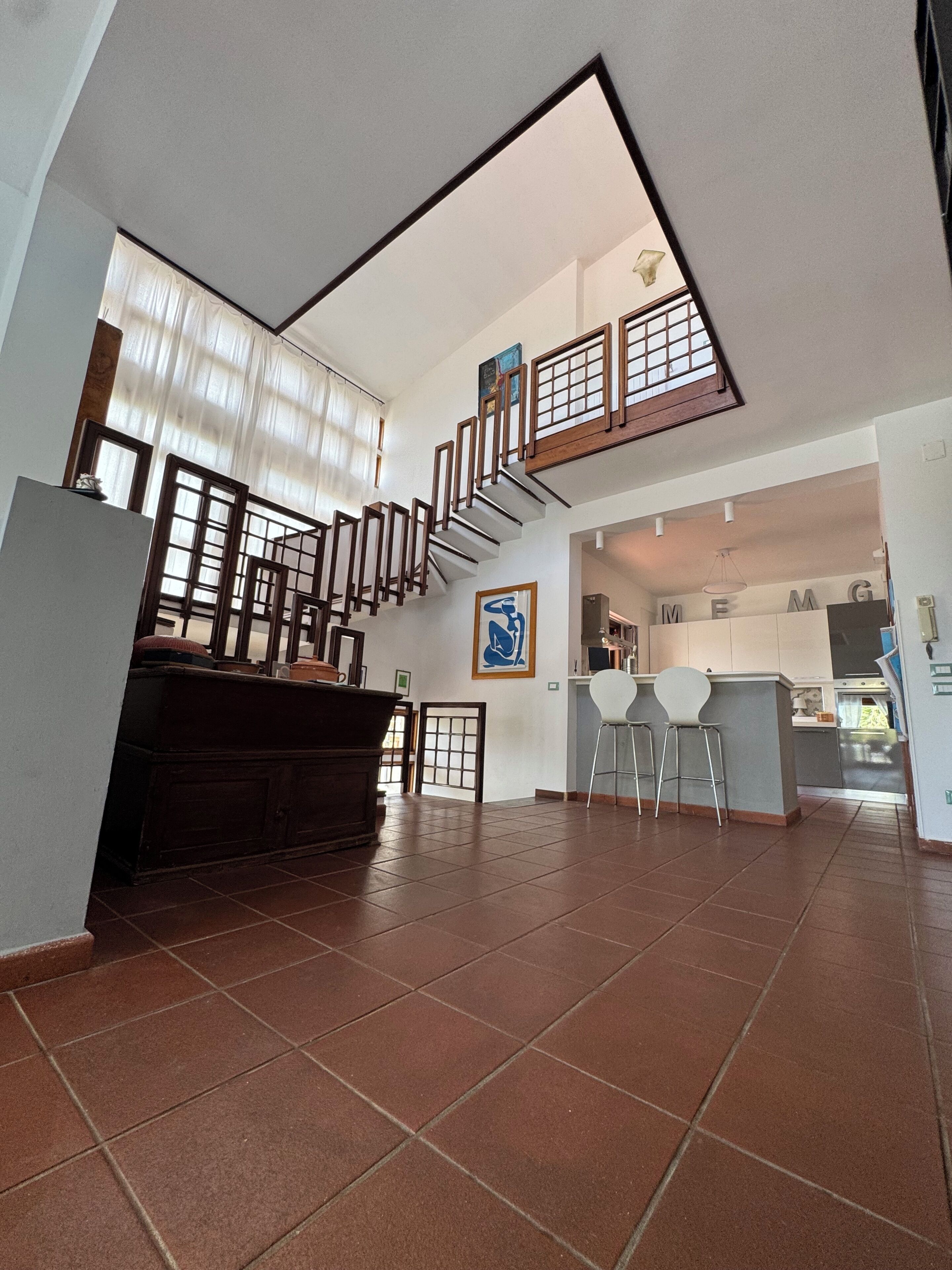 A spacious interior with a staircase leading to a loft area, a kitchen with bar stools, and a dining area with a view of the kitchen.
