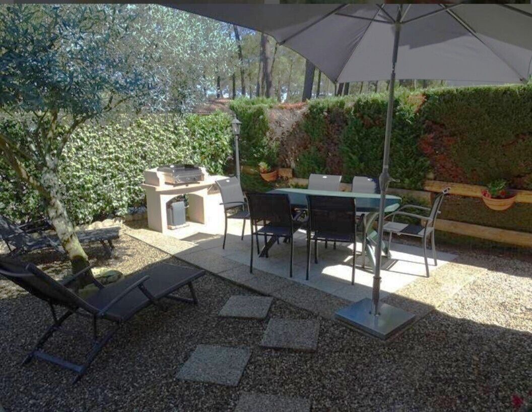 An outdoor patio with a barbecue grill, dining table, chairs, and umbrellas.