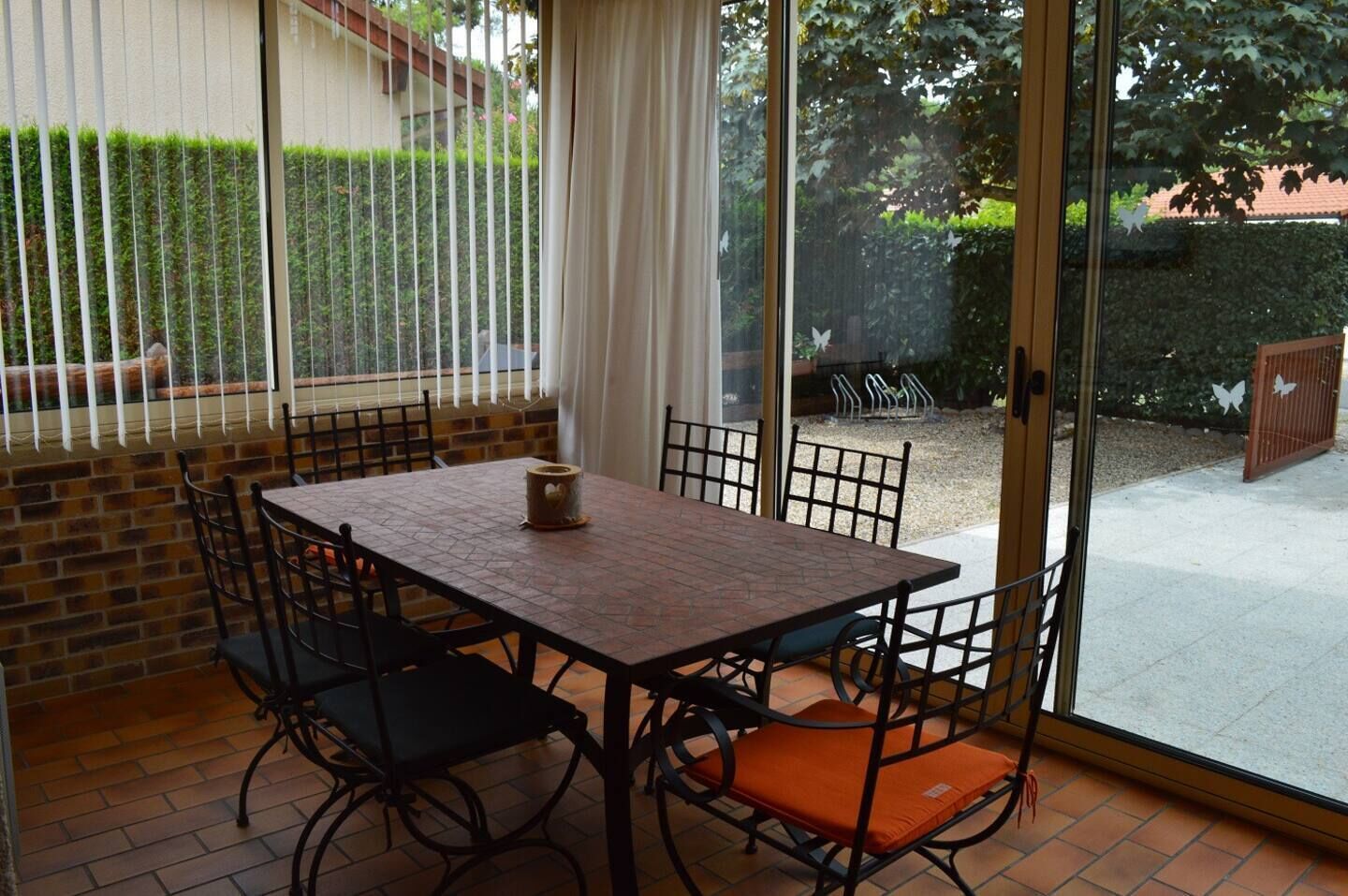 An outdoor patio with a table and chairs, a brick wall, and a view of a garden and house.
