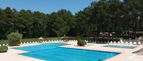 A swimming pool with lounge chairs and a small bridge, surrounded by trees.