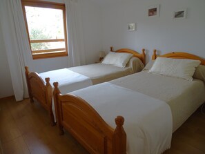 A room with two wooden beds, white bedding, a window with curtains, and a small wall-mounted picture. - Maisonnette de 3 chambres, dans un village vacances à Gujan-Mestras. (Gujan-Mestras)