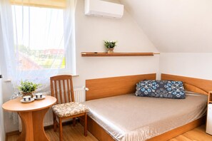 A small, cozy room with a bed, a chair, a small table, and a window with curtains. - Studio for 3 People Close to the sea (Kamien Pomorski)