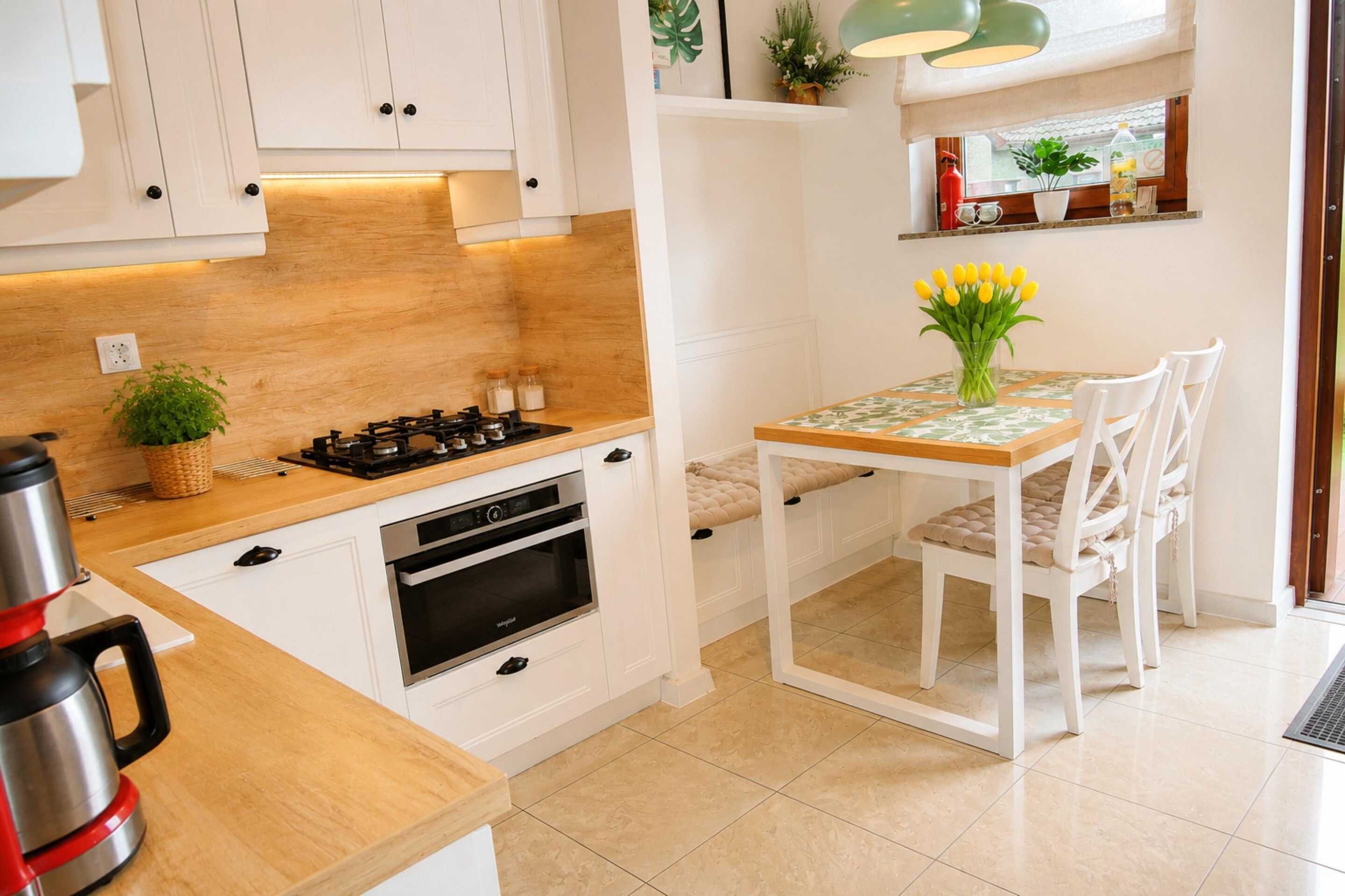A compact kitchen with white cabinetry, a gas stove, an oven, and a dining table with chairs.