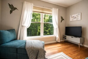 Una sala de estar con sofá, televisión y ventana con cortinas.