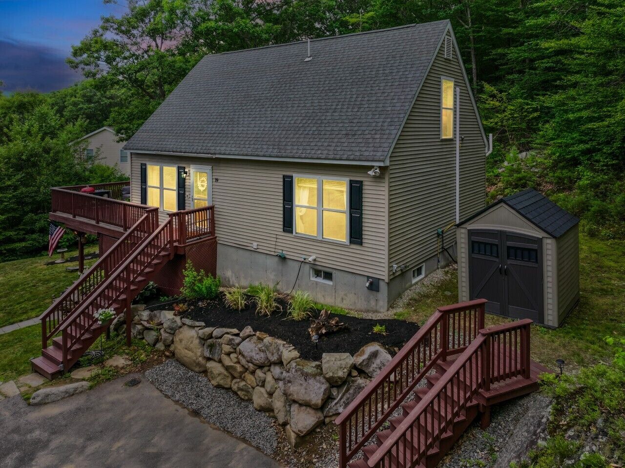 A two-story house with a stone foundation, a wooden deck, and a garage.