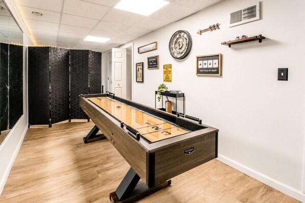 Una habitación con mesa de fútbol, dardos y un reloj en la pared.