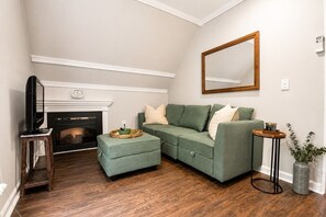 Una sala de estar con chimenea, un sofá verde, un televisor sobre un mueble de madera y un espejo en la pared.