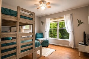 A room with bunk beds, a window with curtains, a ceiling fan, and a desk with a computer.