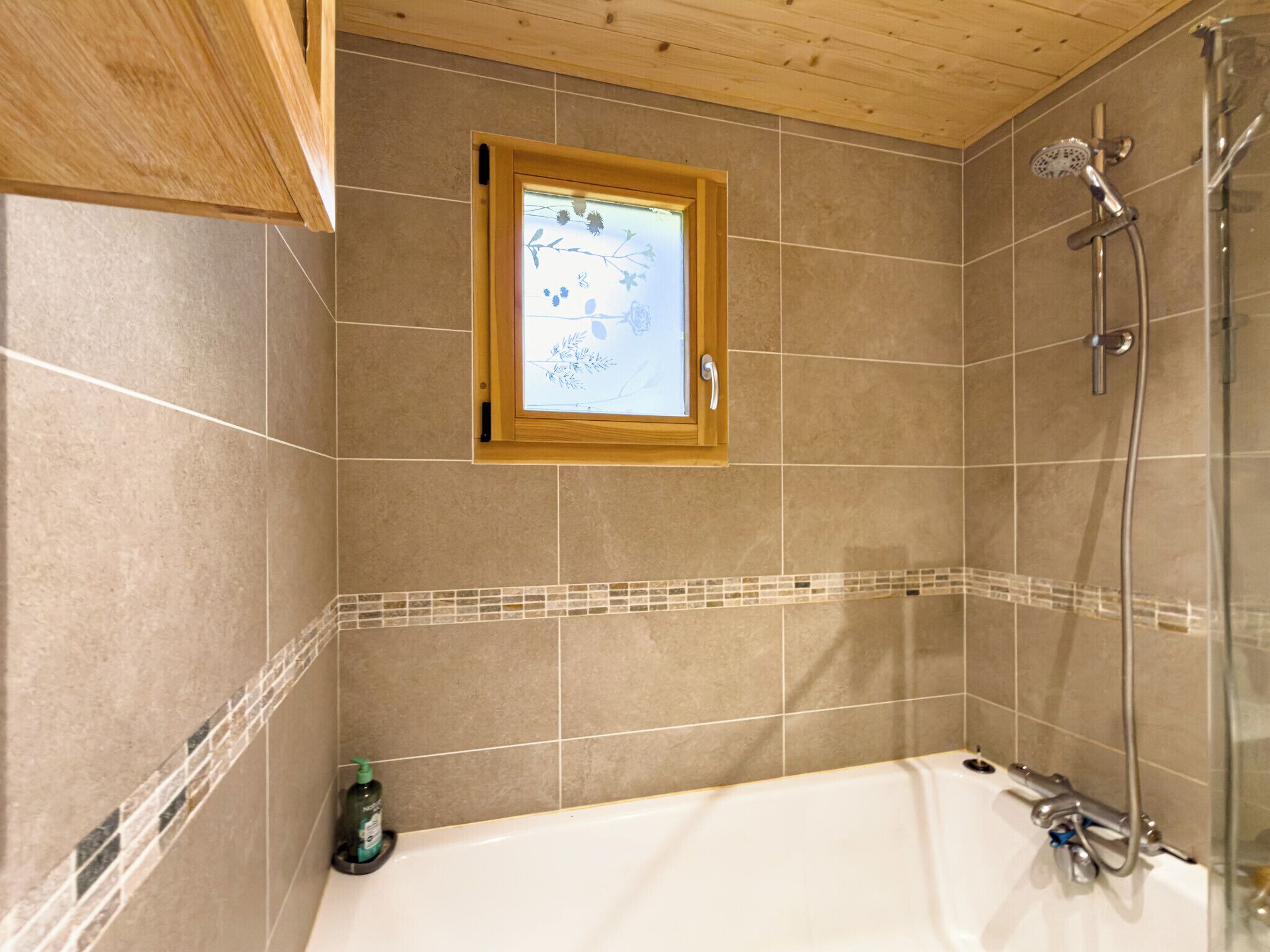 A bathroom with a bathtub, a shower, and a window with a view of nature.