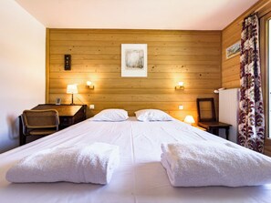 Ein Doppelbett mit zwei Kissen, ein hölzernes Kopfteil, ein Schreibtisch mit Stuhl, zwei Wandlampen und eine Heizung.