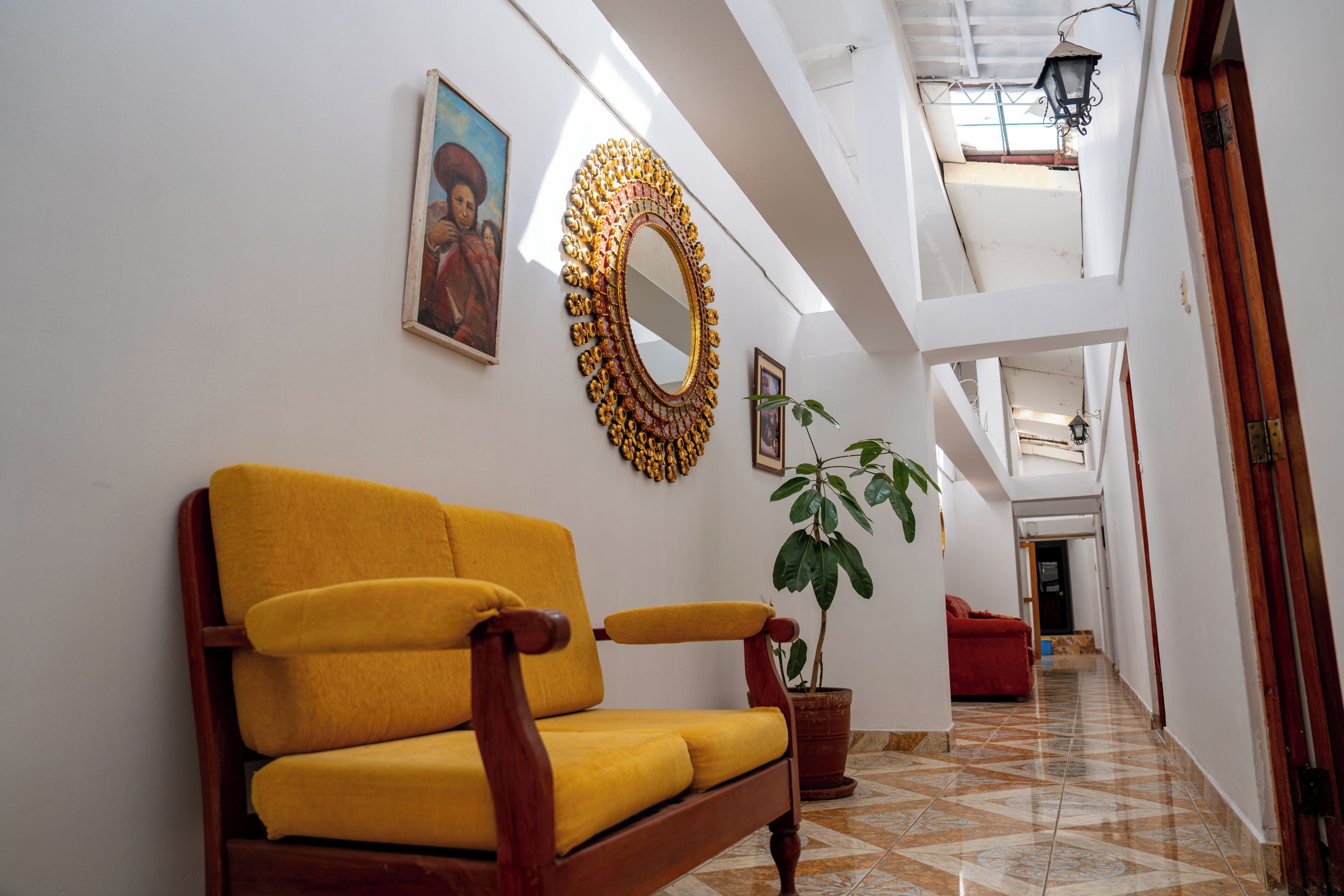 Un couloir avec un canapé jaune, un miroir décoratif et une plante en pot.