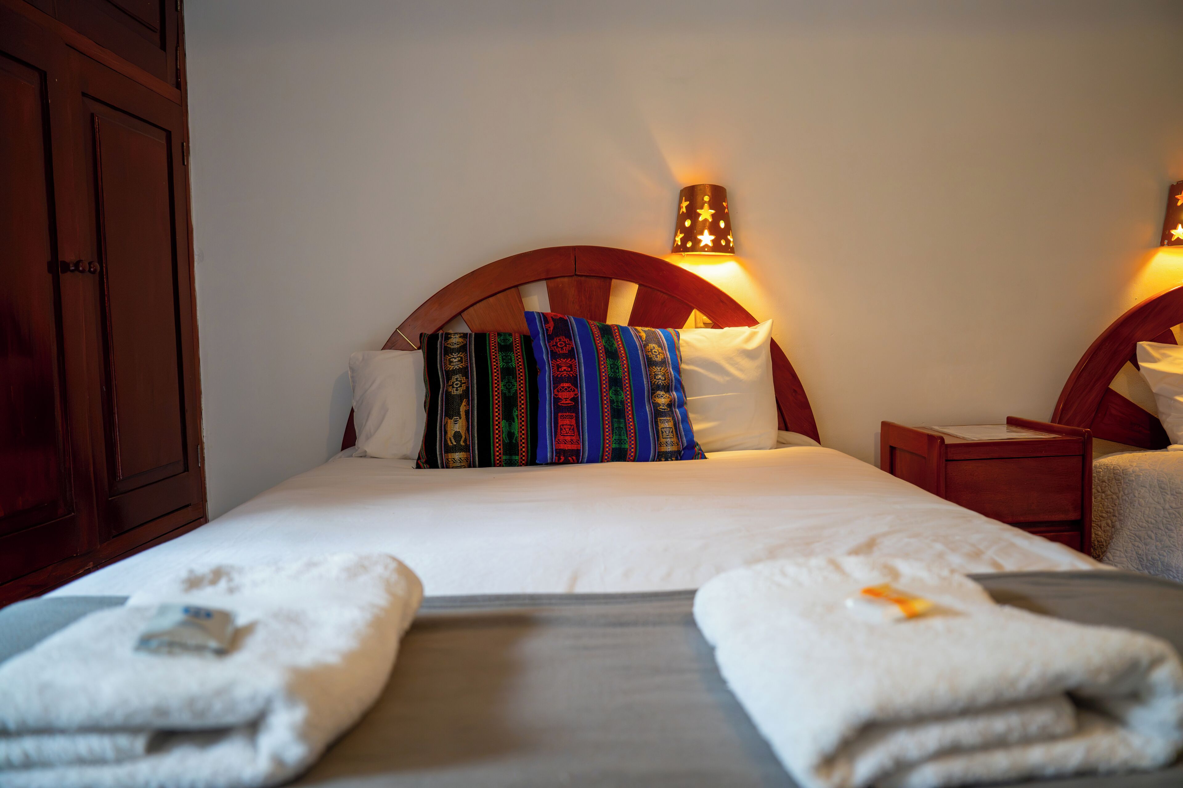 A hotel room with a bed, two bedside tables, a nightstand, and a wardrobe.