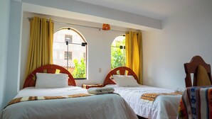 Habitación con dos camas individuales, cada una con cabecero de madera, ropa de cama blanca y vistas a la vegetación a través de ventanas arqueadas.