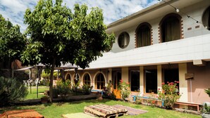 Un patio con zona de estar cubierta, un árbol y un edificio con ventanas arqueadas.
