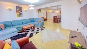 A living room with a sectional sofa, a coffee table, and a dining area with chairs and a table. - Mvuto mzuri Beachfront Apartments (Mombasa)