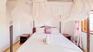 A bed with a canopy, a bedside table, and a window with curtains. - Mvuto mzuri Beachfront Apartments (Mombasa)