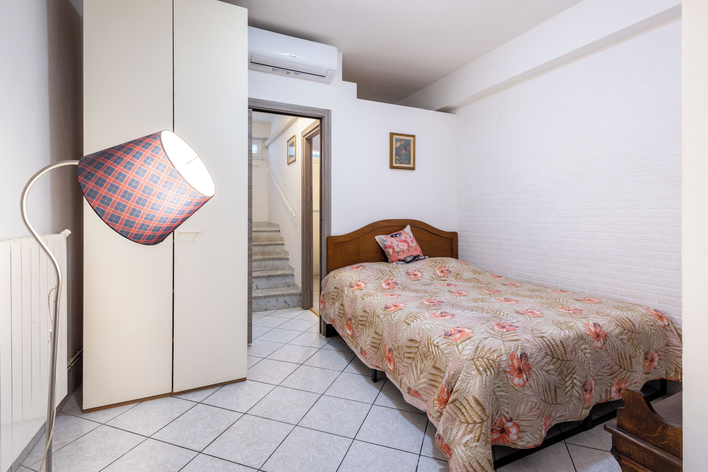Een slaapkamer met een bed, een kledingkast, een deur, een trap en een airconditioner.