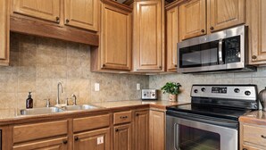 Una cucina con mobili in legno, un forno a microonde in acciaio inox, un tostapane e un fornello.