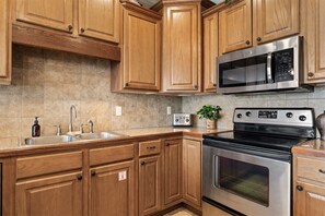 A kitchen with wooden cabinets, a stainless steel microwave, a toaster, and a stove. - The Red Curtain Lakefront (Hollister)