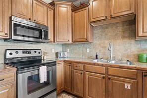 A kitchen with wooden cabinets, stainless steel appliances, a microwave, a stove, a sink, and a green container. - Yakov's Hideaway Lakefront (Hollister)