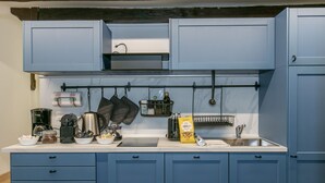 A kitchen with blue cabinets, a countertop with various appliances and utensils, and a hanging rack for pots and pans. - Trevi Little Palace #5 - 52 Steps - no elevator (Rome)