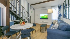 A modern living room with a blue sofa, a round table with chairs, a television, and a staircase with striped walls. - Trevi Little Palace #5 - 52 Steps - no elevator (Rome)