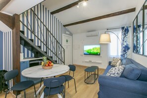 Ein modernes Wohnzimmer mit einem blauen Sofa, einem runden Tisch mit Stühlen, einem Fernseher und einer Treppe mit gestreiften Wänden.