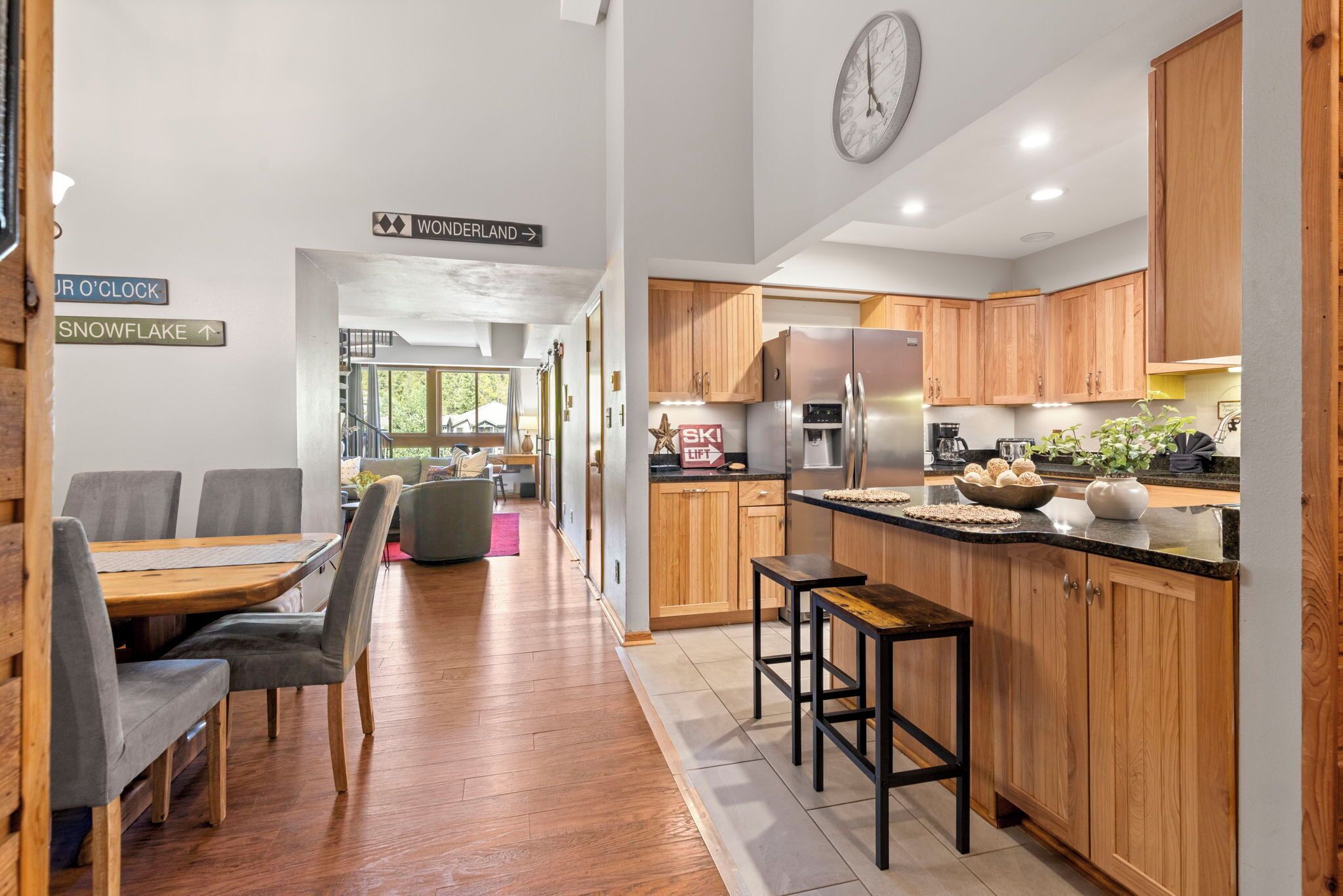 A modern kitchen with wooden cabinets, a stainless steel refrigerator, and a dining area with a table and chairs.
