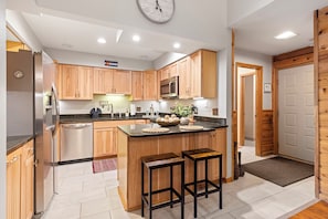 A modern kitchen with wooden cabinets, a stainless steel refrigerator, a microwave, and a clock on the wall. - Walk to Main St & BreckConnect Gondola • Hot Tub & Views • Comfortably Sleeps 10 (Breckenridge)