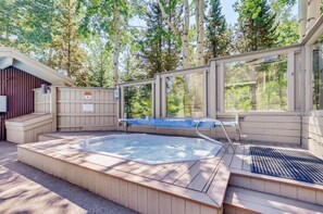 Un espace avec un bain à remous, doté d’une terrasse en bois, entouré d’une clôture en bois et d’arbres.