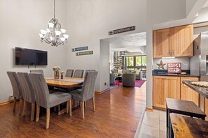 A modern kitchen with wooden cabinets, a dining area with a large table and chairs, a chandelier, and directional signs indicating nearby locations. - Walk to Main St & BreckConnect Gondola • Hot Tub & Views • Comfortably Sleeps 10 (Breckenridge)