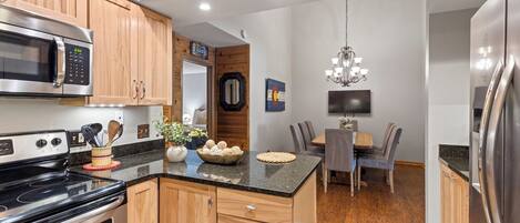A modern kitchen with wooden cabinets, a stainless steel refrigerator, a microwave, and a stove.
