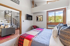 A bedroom with a bed, a sofa, a TV, a mirror, and a window with a view of trees. - Walk to Main St & BreckConnect Gondola • Hot Tub & Views • Comfortably Sleeps 10 (Breckenridge)