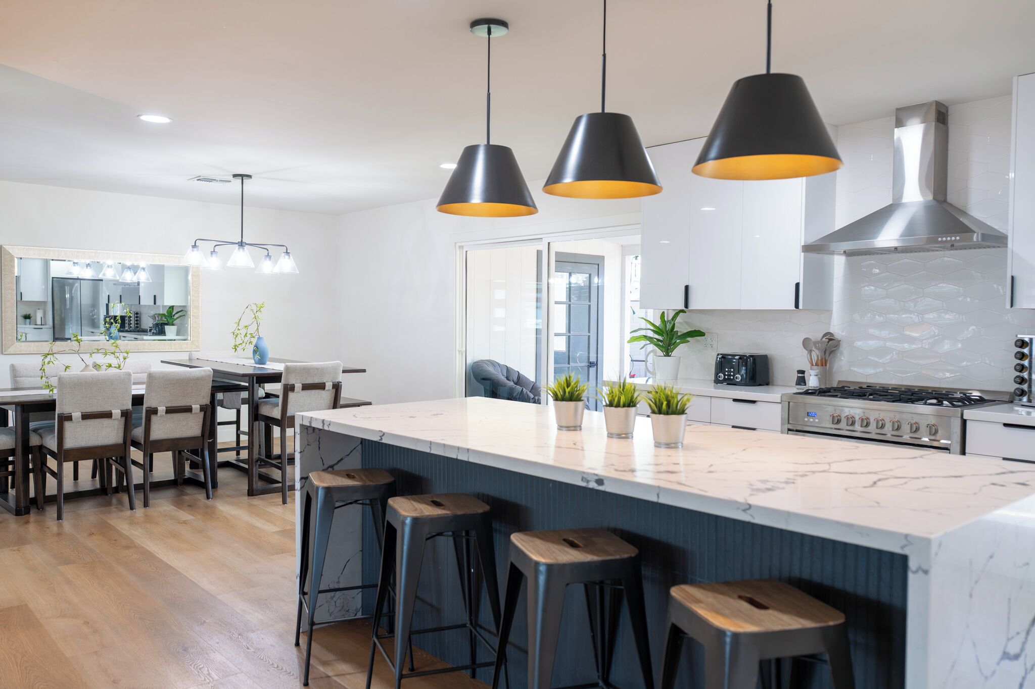 A modern kitchen with a large island, bar stools, pendant lights, and a dining area with a table and chairs.