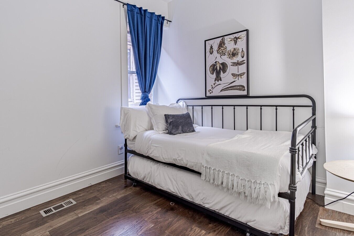 Flexible Sleeping Space: Enjoy a comfortable stay tailored for extra guests or kids in this bright bedroom space, complete with a stylish wrought-iron daybed frame, plush accent pillows, and blackout window coverings for maximum privacy.