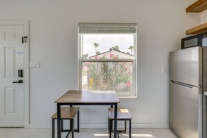 A kitchen with a built-in refrigerator, a window with a view of a house and palm trees, and a table with two chairs. - Beachside Luxe Studio #1 (South Padre Island)
