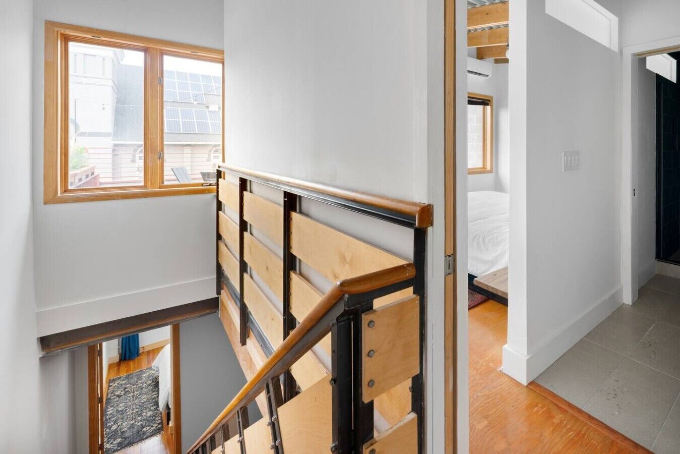 Una escalera con barandillas de madera y vistas a un dormitorio con cama y ventana.